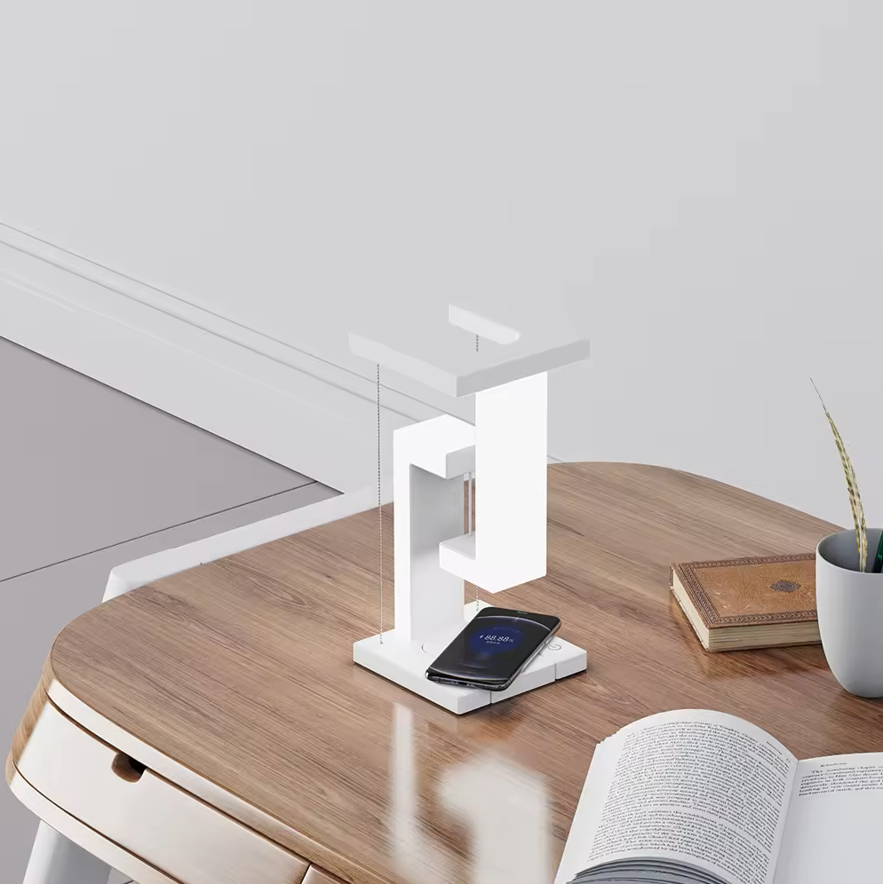 White desk lamp on a wooden desk with a smartphone, open book, and small plant.