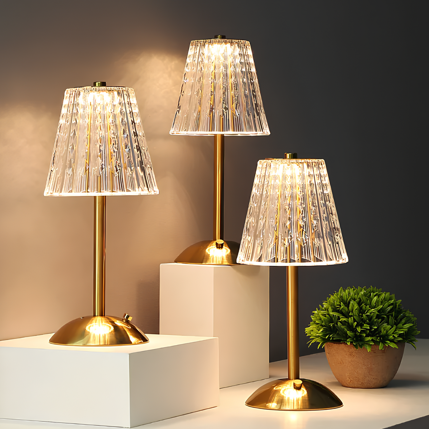 Three decorative table lamps with gold bases and clear glass shades on a neutral background.