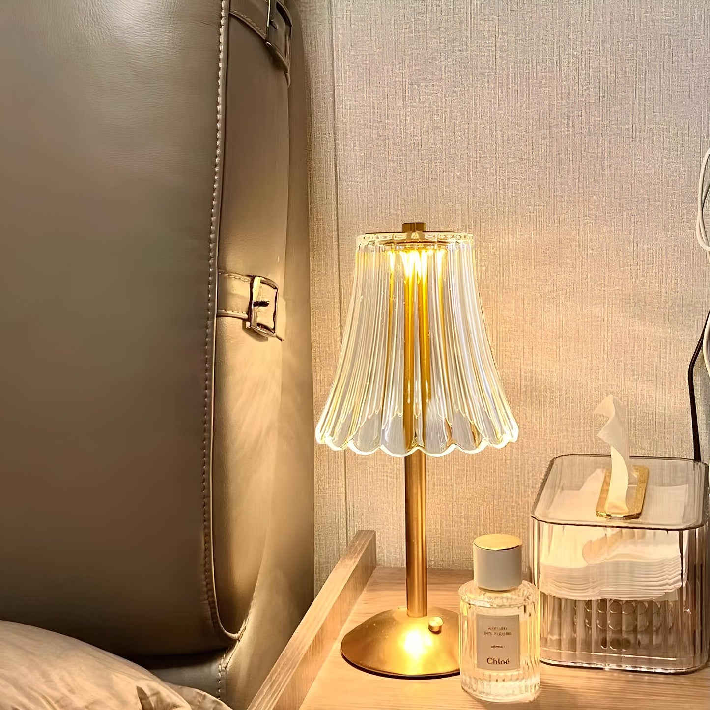 Small table lamp on a bedside table with a bottle of perfume and a glass container.