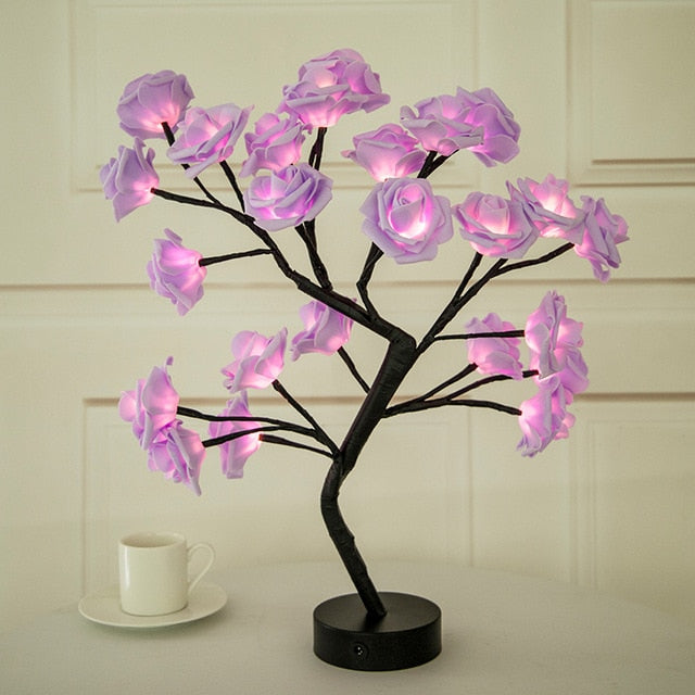 Decorative LED tree with pink flowers on a white surface next to a cup.