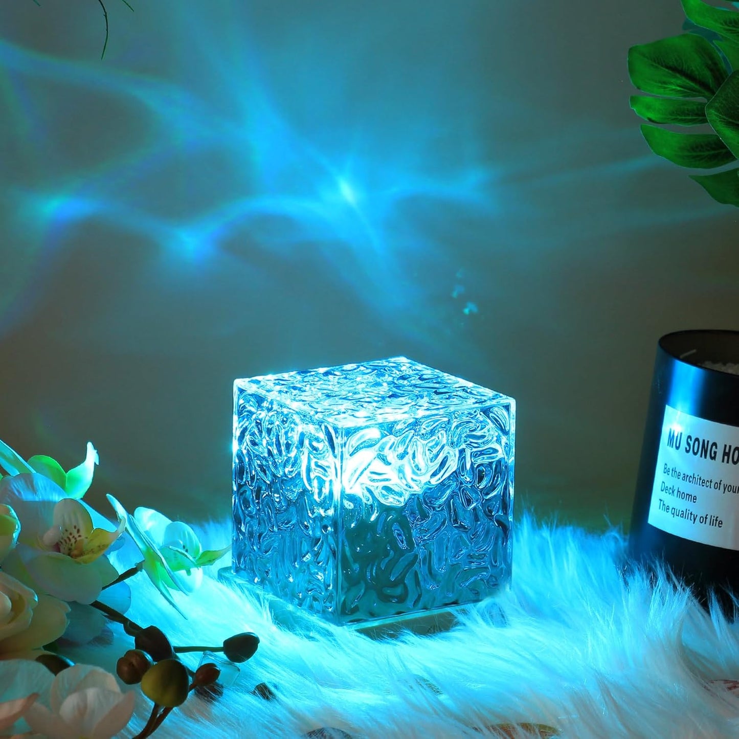 Decorative blue cube light on a surface with plants and a bottle in the background