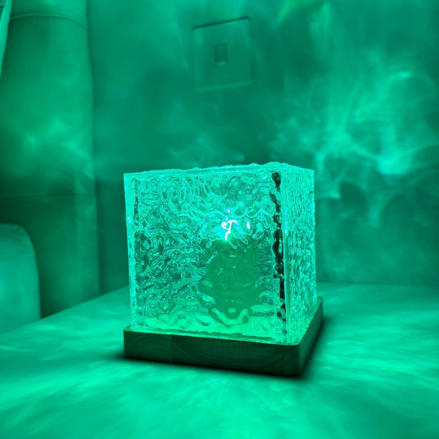 Glass block with textured surface on a stand, emitting a green glow against a green background