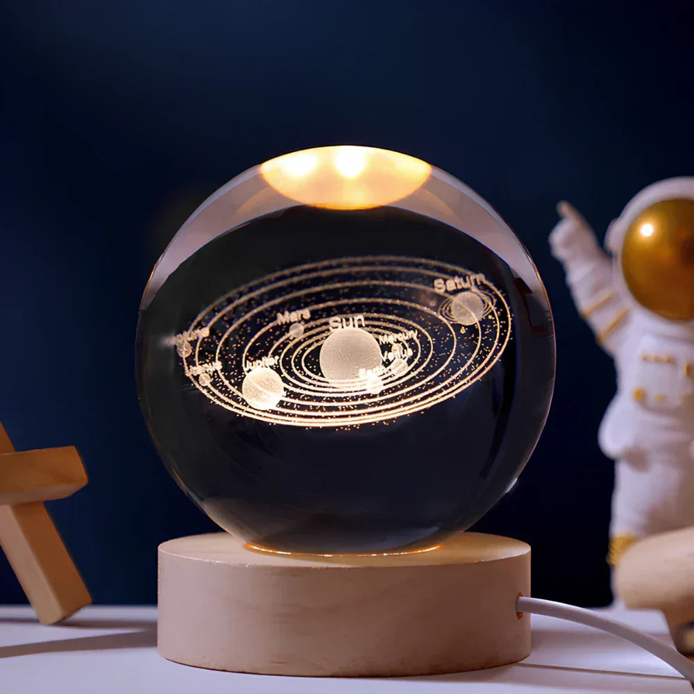 Glass ball with solar system model on a wooden base, illuminated against a dark background.