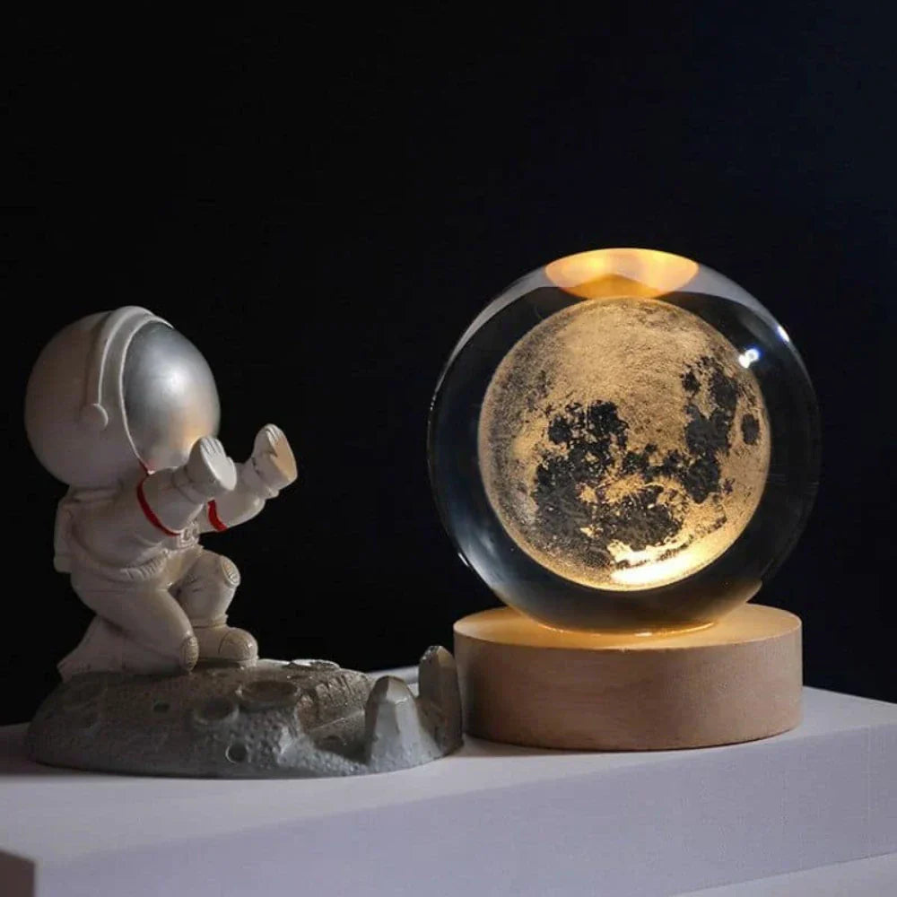Model of an astronaut on the moon next to a glass ball displaying the moon's surface.