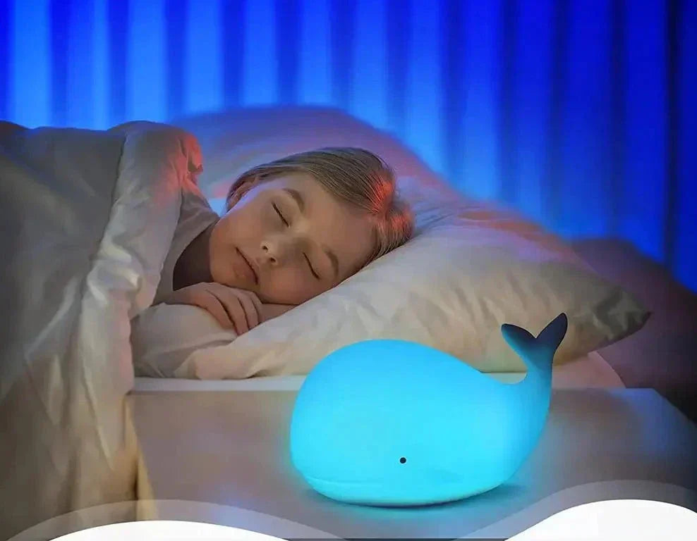 Child sleeping with a whale-shaped night light on a bed