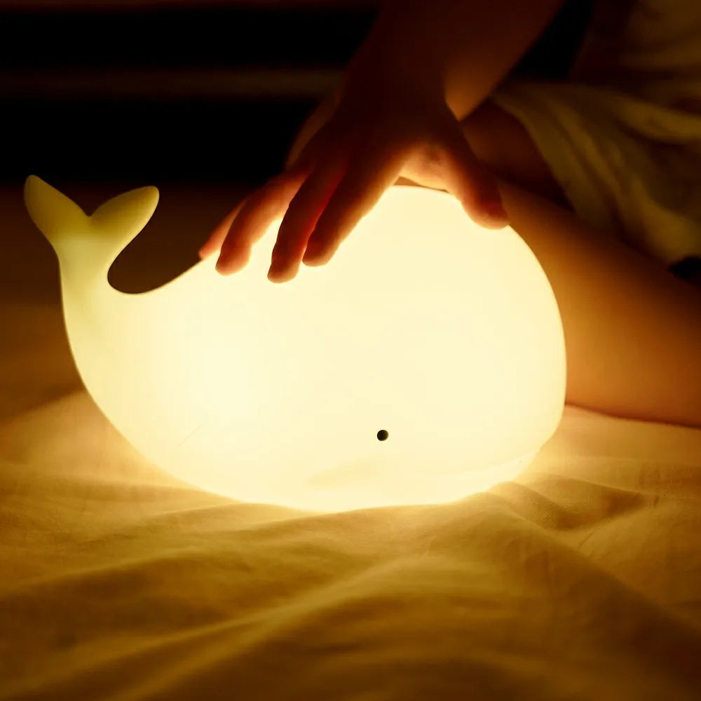 Whale-shaped night light being held by a child's hand on a soft surface