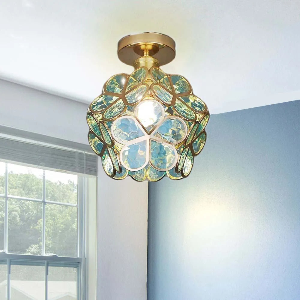 Decorative ceiling light fixture with green and gold design in a room with a window.