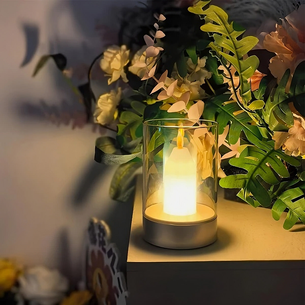 Candle in a glass holder on a table with plants in the background