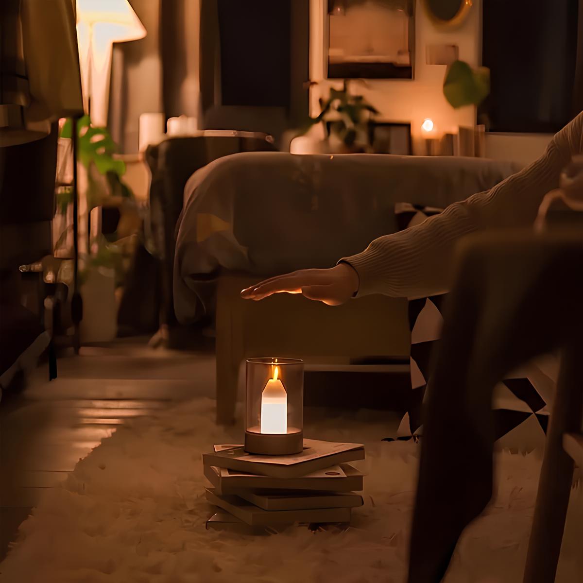 Person holding an outstretched hand towards a lit candle on a stack of books in a dimly lit room.