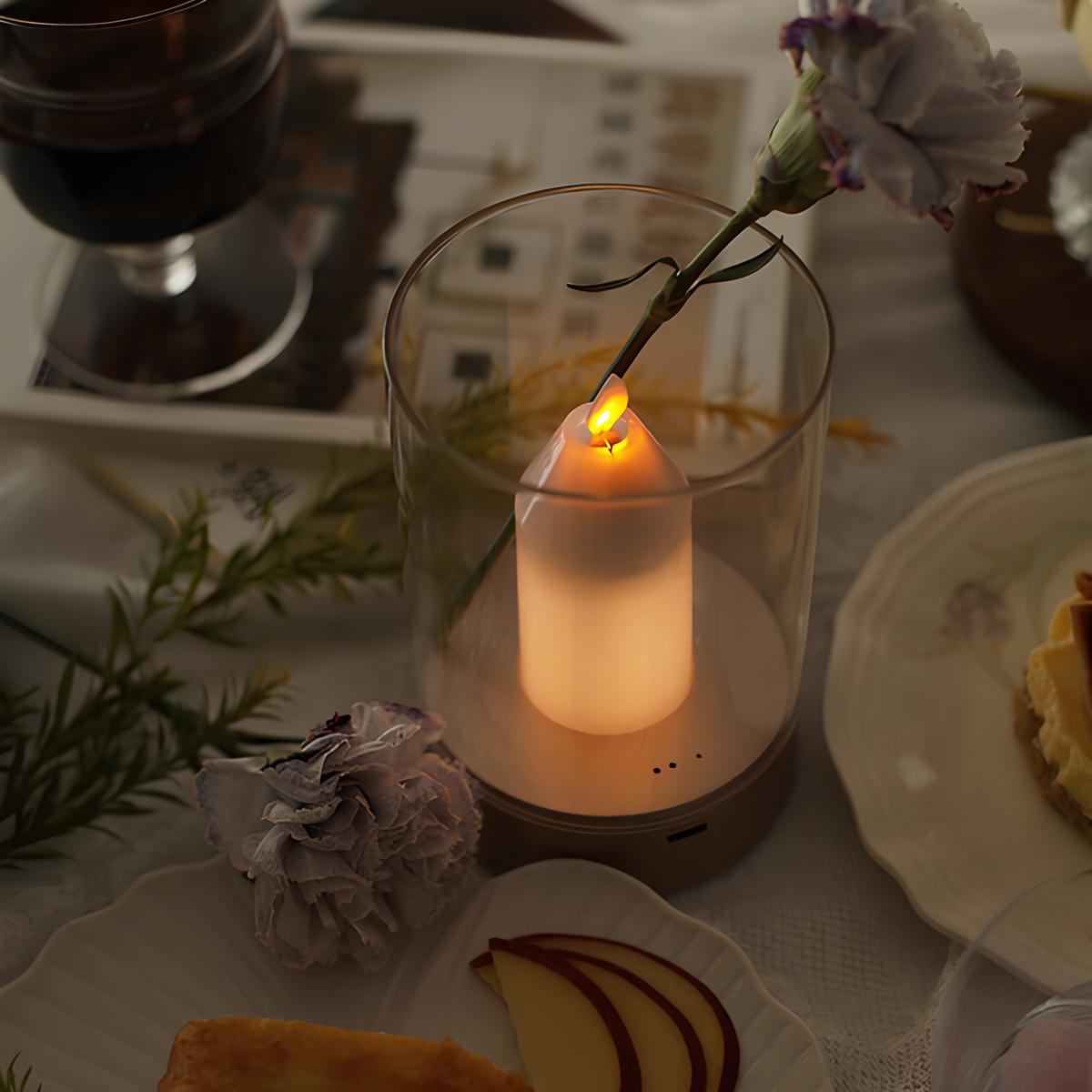 Candle in a glass holder on a table with food and flowers