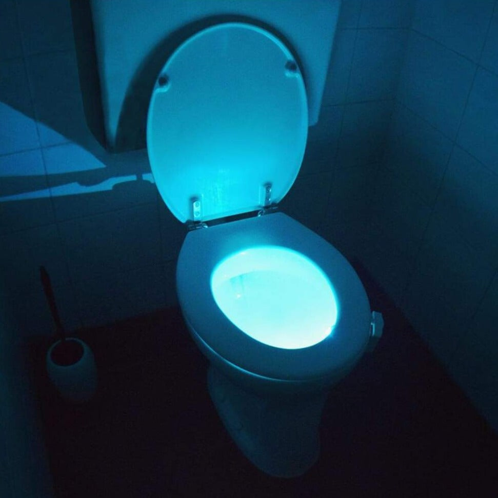 Toilet with glowing seat in a dark bathroom