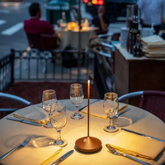 Dining table set with glasses, candles, and cutlery in an outdoor restaurant setting.