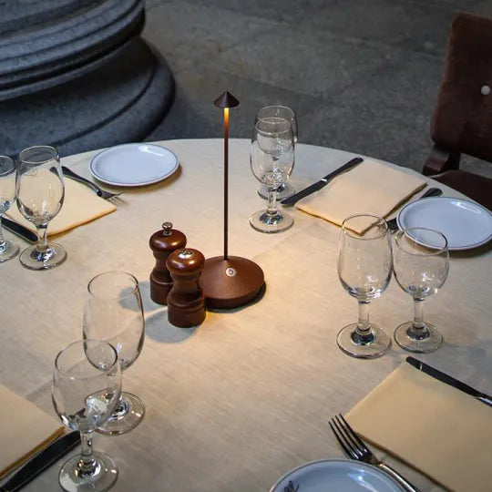 Dining table setup with wine glasses, plates, cutlery, and a small lamp.