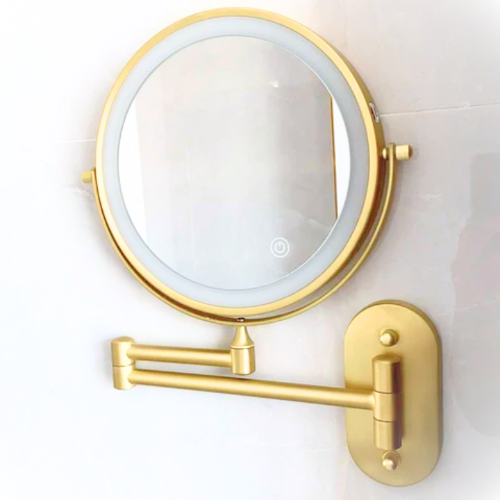 Gold wall-mounted makeup mirror with light on a white background