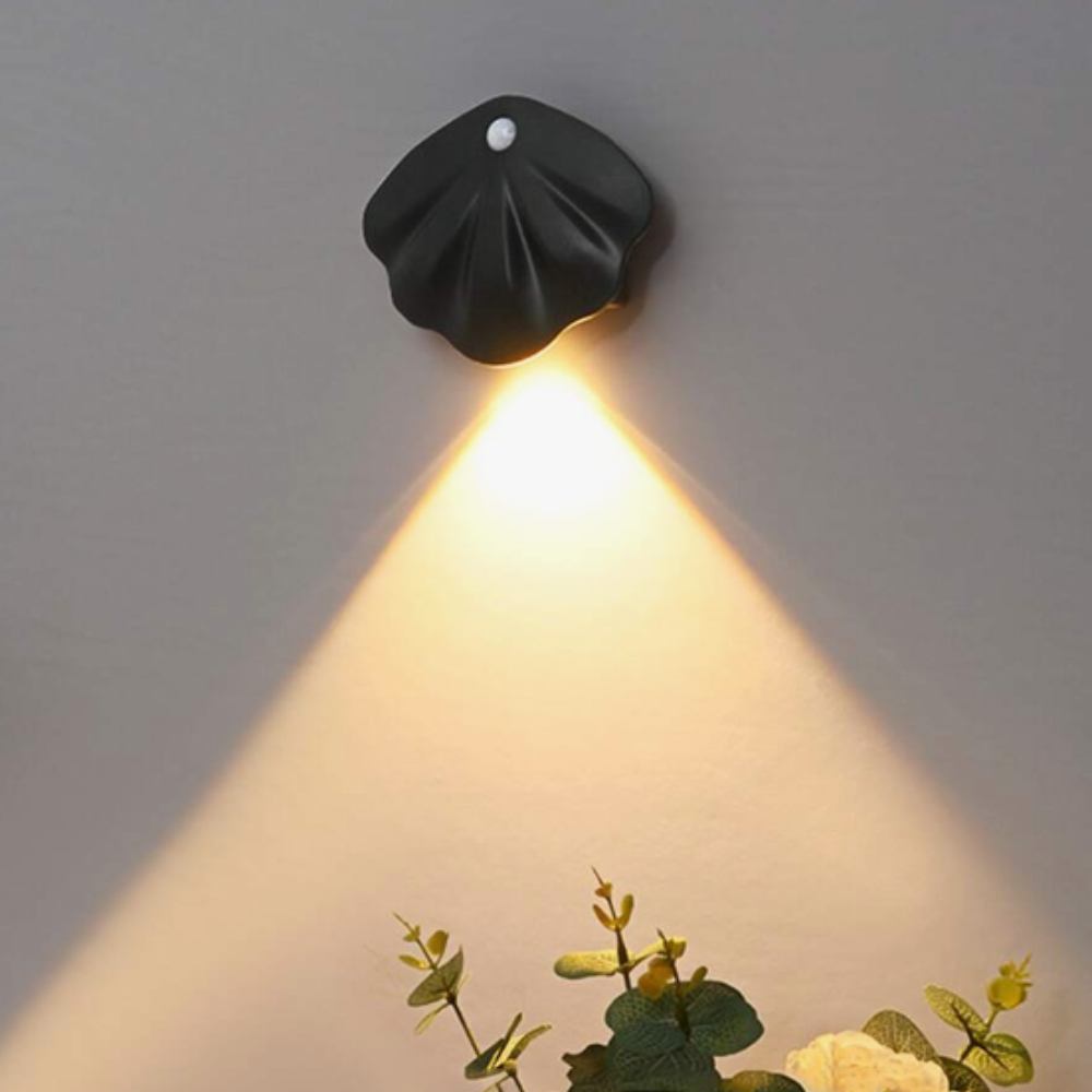 Black wall-mounted light fixture on a gray wall with a plant in the foreground.