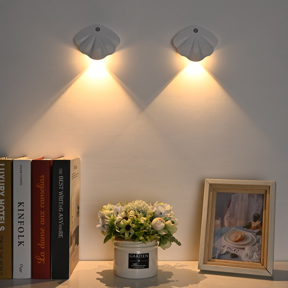 Shell-shaped wall lights on a wall with books, a plant, and a photo frame below.