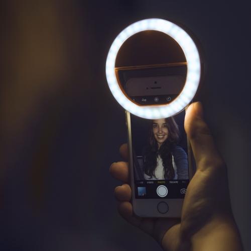 Hand holding a smartphone with a ring light in a dark setting