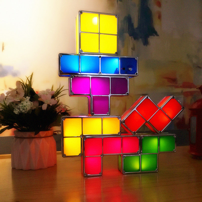 Colorful Tetris-style lamp on a wooden surface with flowers in the background