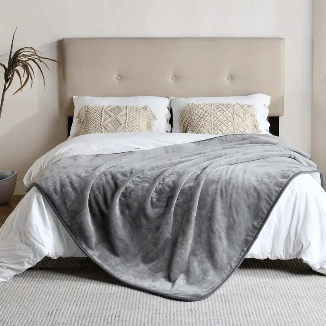 Gray blanket draped over a bed with white bedding and patterned pillows in a bedroom setting.