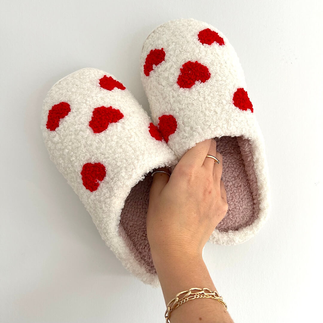 White slippers with red heart patterns worn by a person on a light gray background