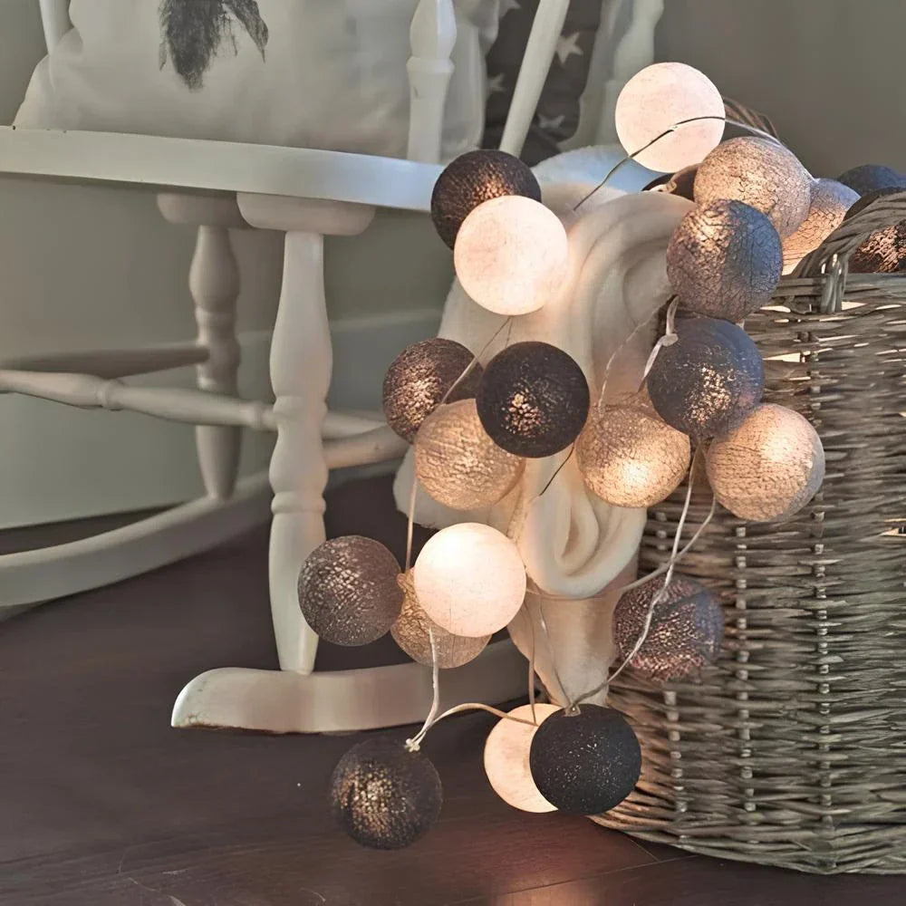 String lights with black and gold balls on a wooden surface next to a white chair.