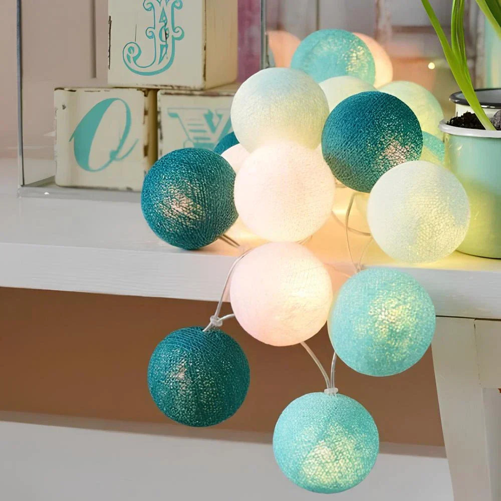 String lights with teal and white balls on a surface with decorative items in the background.