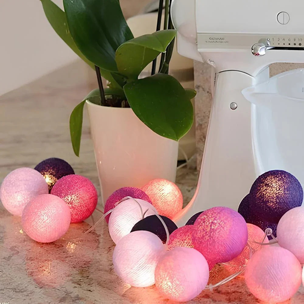 String of colorful cotton ball lights on a kitchen counter with a plant and mixer in the background.
