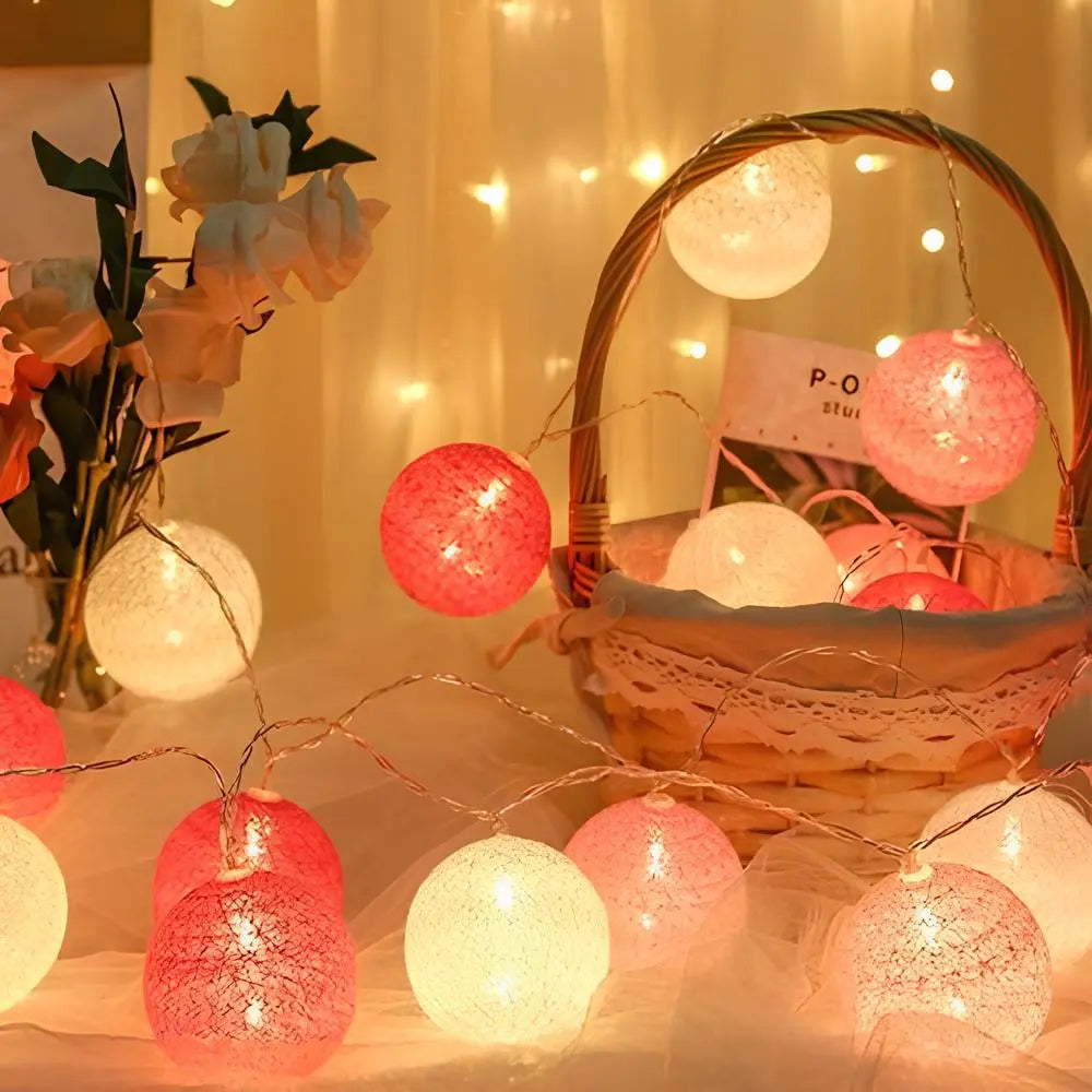 String lights with colorful lanterns on a table with a basket and flowers in the background.