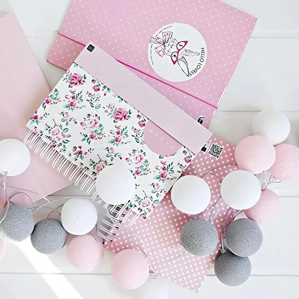 Decorative stationery items including a floral notebook, pink polka dot paper, and string lights on a white surface.