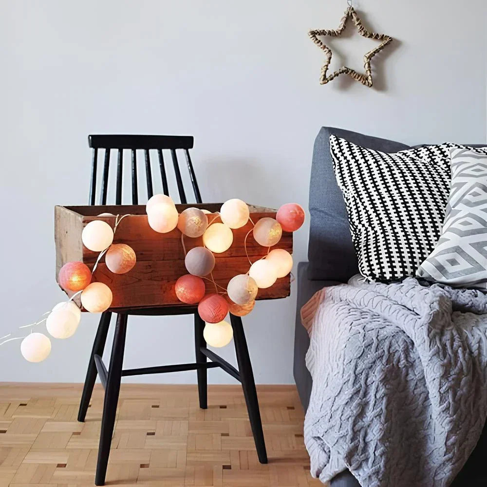 String lights on a wooden stool next to a bed with pillows and a blanket.