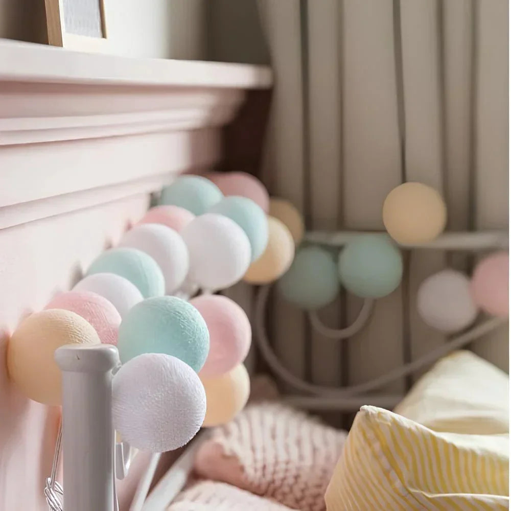 Pastel-colored pom-pom garland hanging on a shelf with a soft focus background.