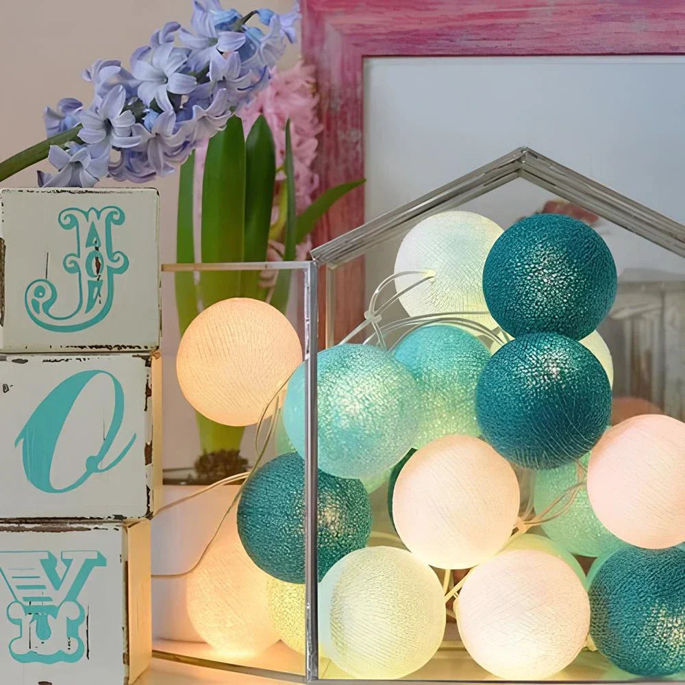 String lights with teal and white balls in a decorative setting with flowers and wooden blocks.
