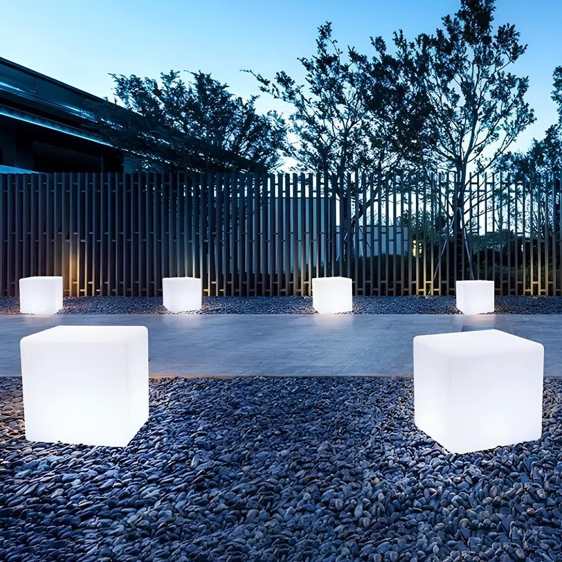 White cubic light fixtures on a gravel surface with trees and a building in the background.