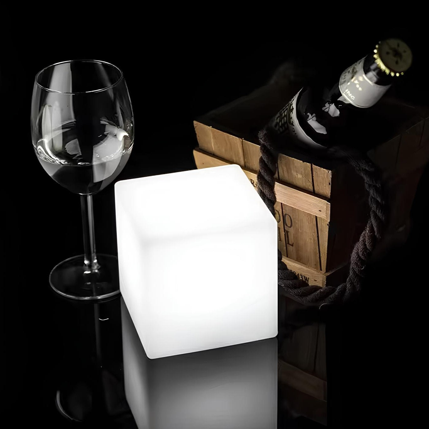 Glowing cube light next to a wine glass and bottle on a dark background
