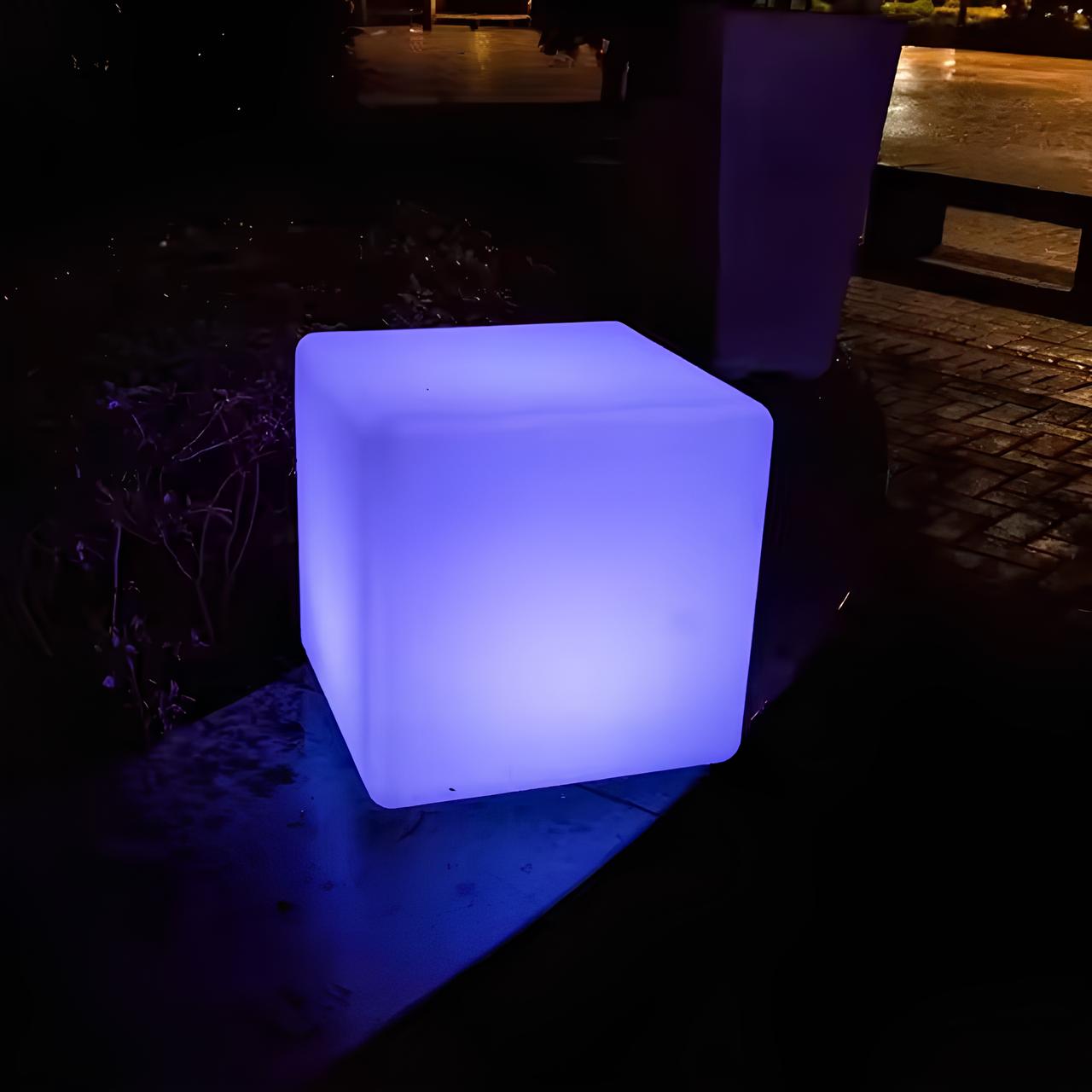 Cube-shaped illuminated stool glowing blue on a dark outdoor setting