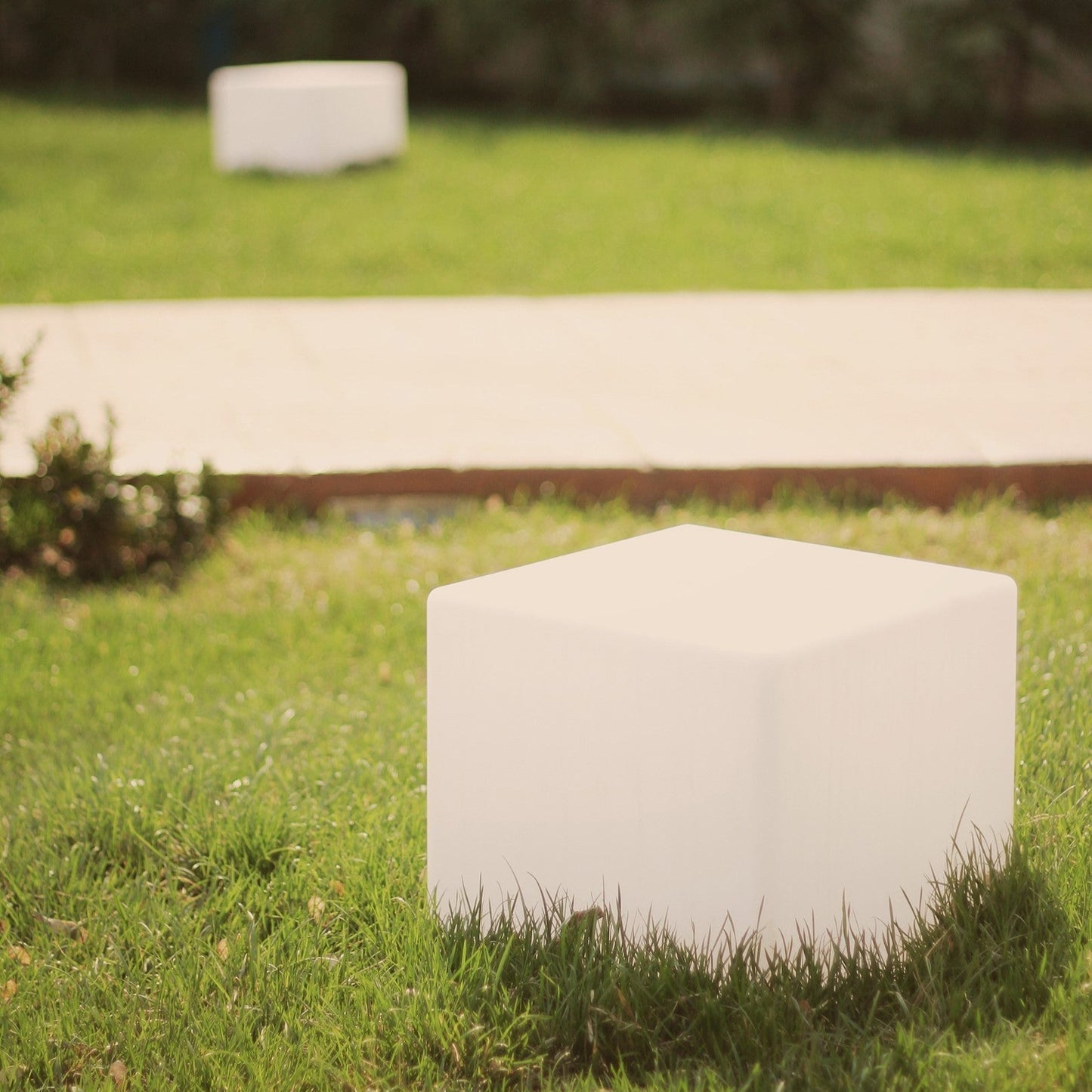 White stone monument in a grassy area with a blurred pathway and trees in the background