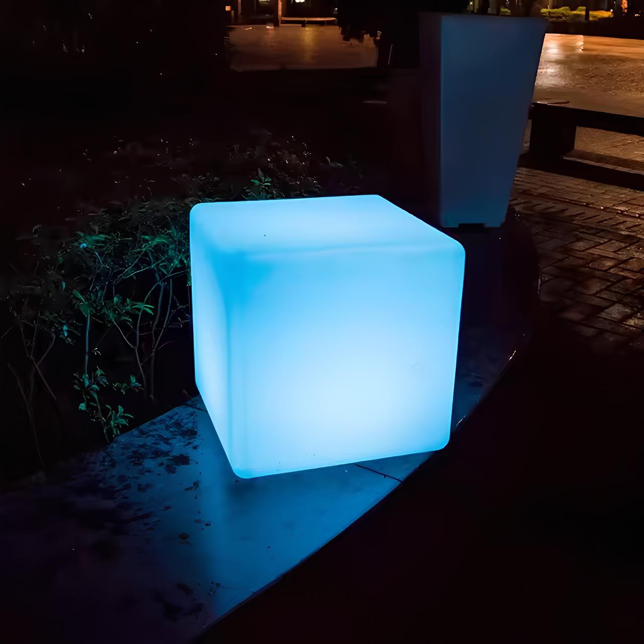Blue illuminated cube on a dark outdoor surface