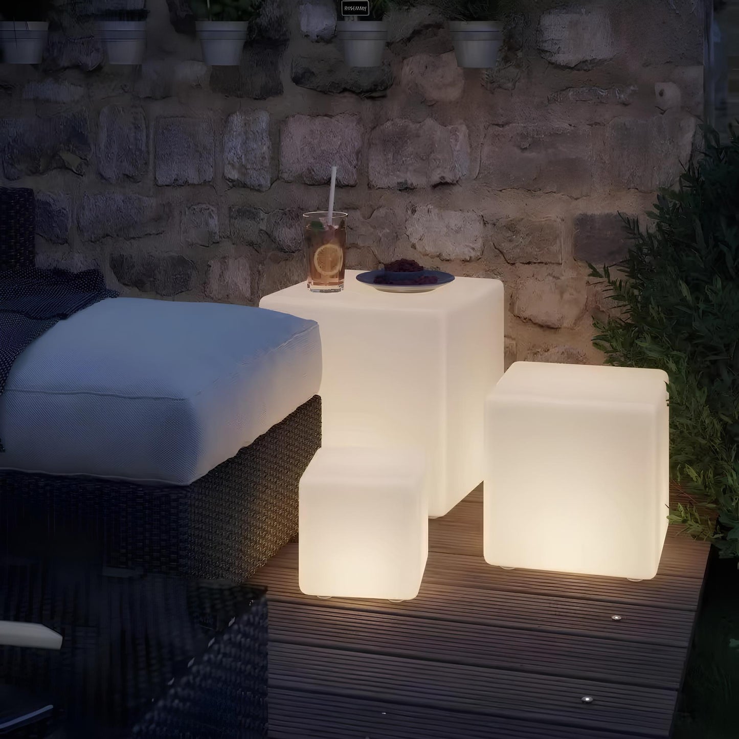 Outdoor setting with illuminated cube-shaped lamps against a stone wall.