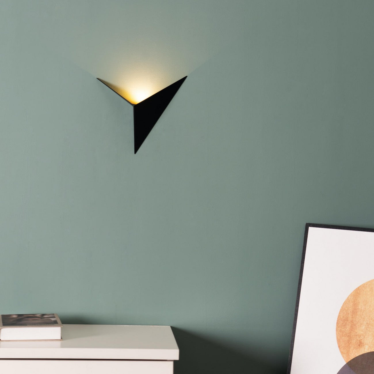 Modern black wall sconce on a green wall with a piece of abstract art in the corner.