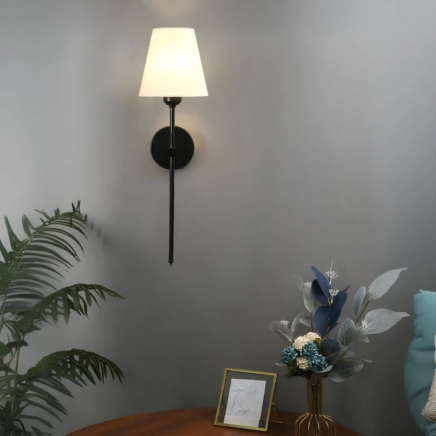 Josh & Tate - LumaElegance Wireless Wall Lamp - Wall-mounted lamp with a plant and decorative items on a table against a gray wall.