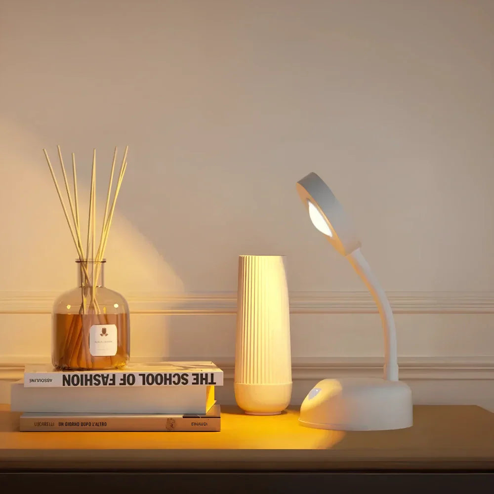 White desk lamp on a wooden surface with decorative items including books and a vase.