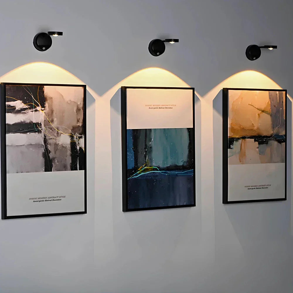 Three framed artworks on a wall with lighting fixtures above.