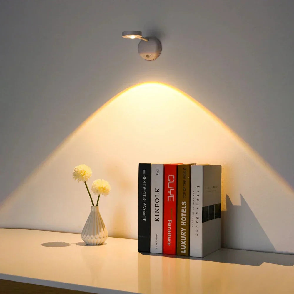 Wall-mounted light fixture casting a warm glow on books and a vase with flowers on a shelf.