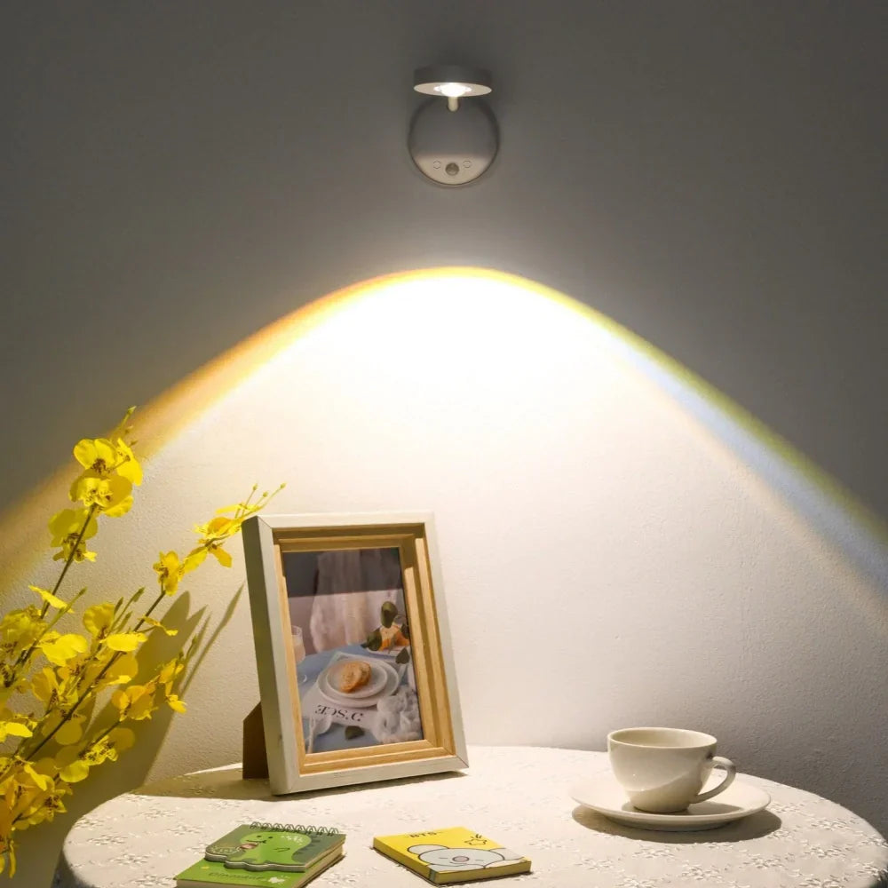 Wall-mounted light fixture casting a warm glow on a table with a photo frame, cup, and flowers.