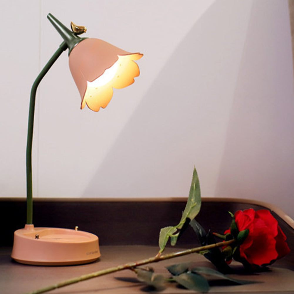 Small lamp with a pink shade on a surface next to a red rose.