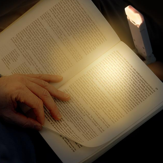 Open book with a hand holding it, illuminated by a small lamp in a dark setting