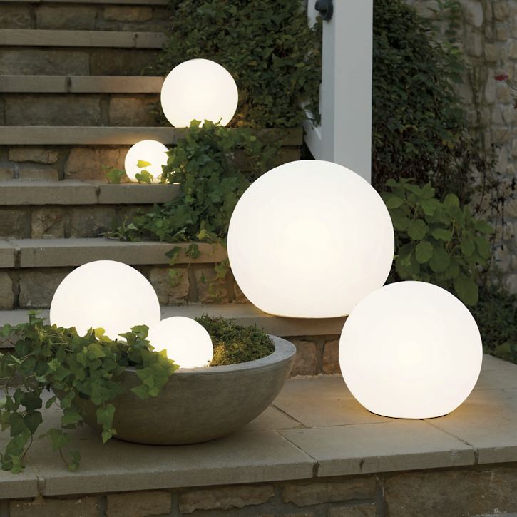 Glowing spherical outdoor lights on a stone ledge with plants.