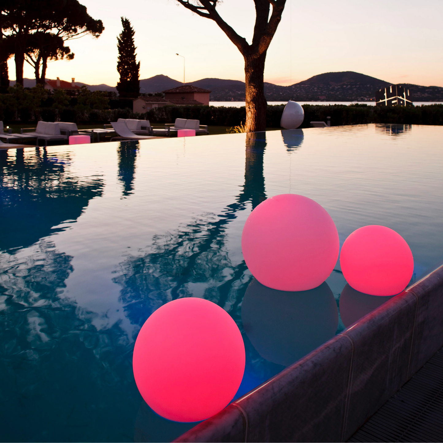 Pink floating lights in a pool with a scenic background