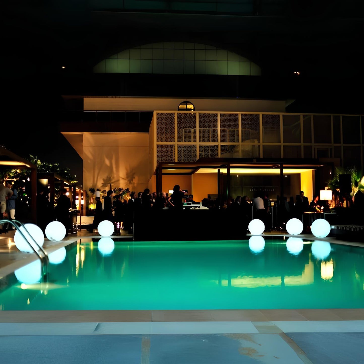 Pool area with illuminated balloons at night, people around, and building in the background.