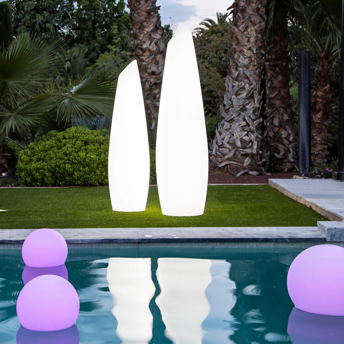 Two tall white outdoor lamps and purple漂浮球 in a pool with palm trees in the background